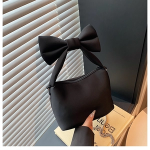 Close-up of matte black handbag featuring a large bow handle and silver chain detail