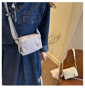 Detailed view of light gray nylon crossbody bag with side woven label and wide strap