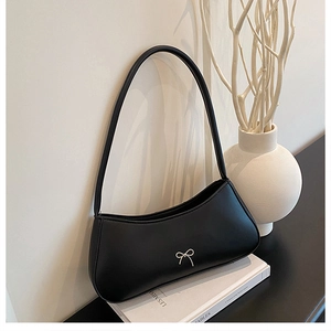 Detail of minimalist black underarm bag with a delicate silver bow on matte material