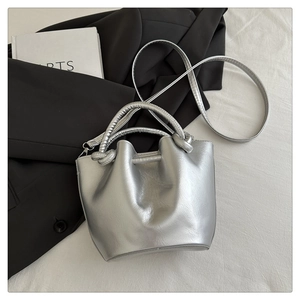 Detail of silver bucket bag with metallic finish and unique knotted handle on white fabric