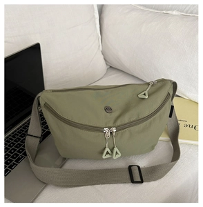 Detail of olive green nylon sling bag featuring double zippers and wide adjustable strap