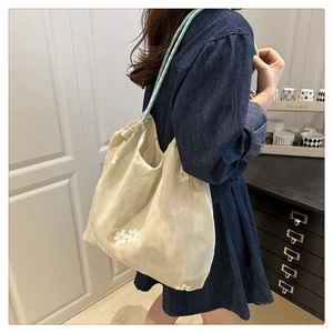 Detailed embroidery on a beige mesh tote bag held by a model in a cozy interior