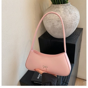 Detail of light pink shoulder bag with a silver bow buckle held by a model
