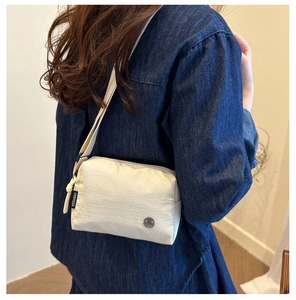 Detail of FANYISSA cream nylon crossbody bag with side woven label and metal logo emblem
