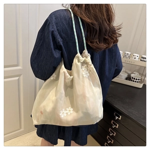 Detail of cream tulle shoulder bag featuring white flower embroidery and drawstring closure