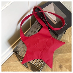 Flat lay of a red star shaped crossbody bag on a metallic suitcase with a wide strap