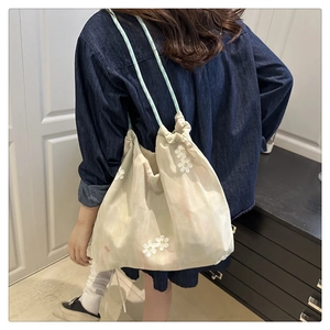 Detail of beige bucket tote featuring daisy floral embroidery and blue drawstring handle