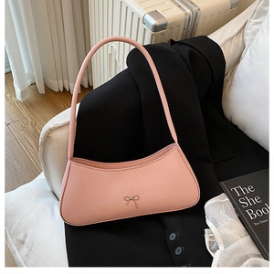 Detail of pink PU leather baguette bag featuring a metallic bow and elegant shoulder strap