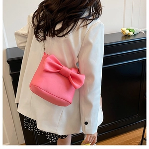 Detail of bright pink bow shoulder bag with silver chain strap worn with white suit