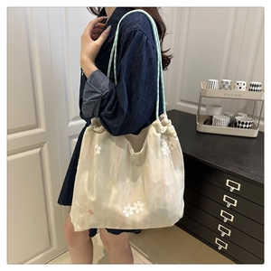 Detail of off-white semi-transparent tote bag with 3D floral embroidery and green rope handle
