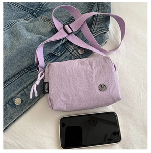 Lilac nylon crossbody bag detail showing logo badge and size scale with a smartphone