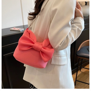 Détail du sac à main rose à nœud avec bandoulière chaîne sur un blazer blanc