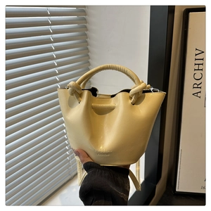 Detail of light yellow bucket bag featuring knotted handle and embossed logo branding