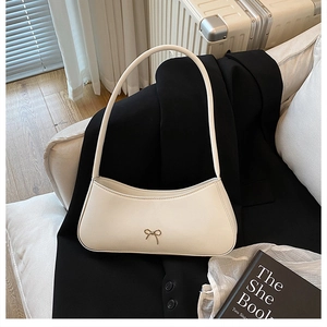 Detail of creamy white crescent bag featuring a delicate gold bow and premium leather texture