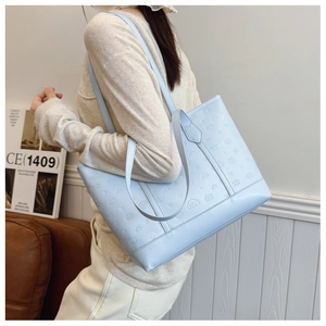 Close-up of light blue tote bag featuring embossed cartoon motifs and long shoulder straps