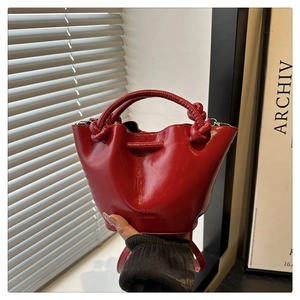 Close-up of bright red glossy bucket bag featuring knot handle and embossed logo detail