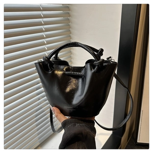 Detail of a black glossy bucket bag with ruched design and decorative knotted handle