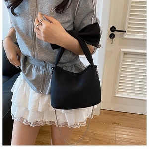 Detail of a black canvas shoulder bag featuring a large bow and silver chain strap