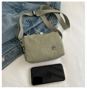 Detail of green nylon crossbody bag next to a phone showing compact size and M logo