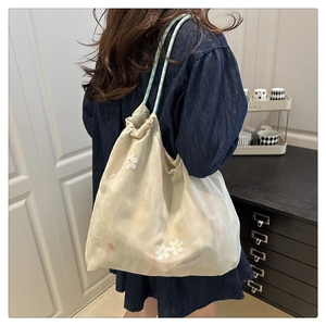Detail of floral embroidered tote bag featuring drawstring closure and slim green straps
