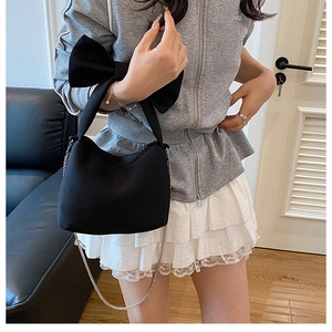 Detailed view of the large decorative bow and silver metal chain strap on black handbag