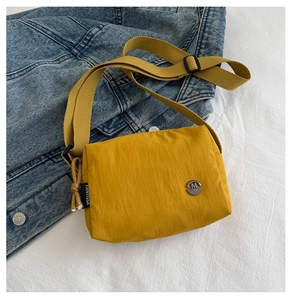 Detail of yellow nylon crossbody bag with flap and black woven side label and logo