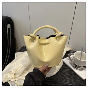 Detail of butter yellow pleated bucket bag showing the glossy patent leather and knotted handle