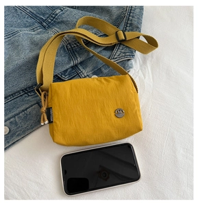 Detailed close-up of yellow lightweight crossbody bag with metal logo and adjustable strap