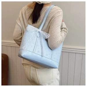 Detail of light blue tote bag featuring embossed characters and white lace bow accessory