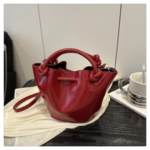 Detail of red glossy bucket bag with knotted handle and embossed logo on black table