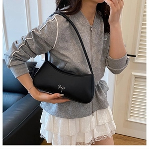 Detail der schwarzen matten Ledertasche mit weißer Schleife am Modell in legerer Umgebung