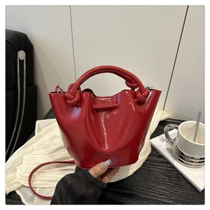 Detail of red glossy patent leather bucket bag with a unique knotted handle design