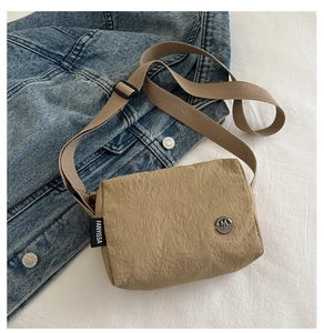 Detail of beige crossbody bag with pleated texture and adjustable nylon strap on denim back