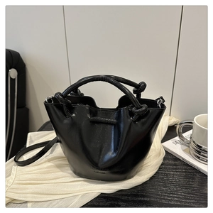 Detail view of black glossy bucket bag featuring a unique knotted handle and brand logo