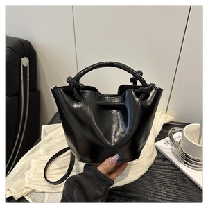 Detail shot of a black pleated bucket bag with a cylindrical handle in a minimalist setting