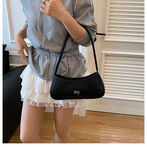 Fashionable black shoulder bag with silver bow detail worn by a model in a cozy setting