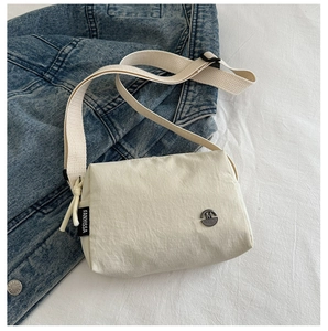Detailed close-up of a beige nylon crossbody bag with wide woven strap on denim jacket