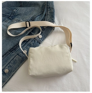 Detailed top view of a minimalist cream nylon crossbody bag with adjustable strap on denim