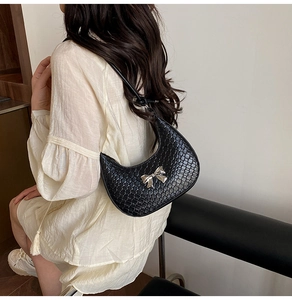Macro detail of black woven crescent bag featuring a metallic silver bow clasp decoration