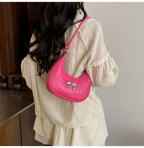 Detail of hot pink woven crescent bag with silver bow buckle on model shoulder