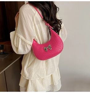 Detail of pink woven crescent bag with silver bow accent on model's shoulder