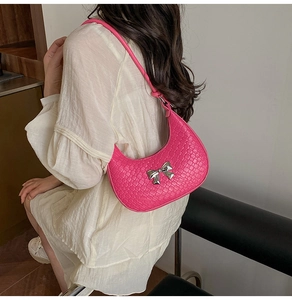 Close-up of bright pink woven crescent bag featuring a metallic silver bow detail