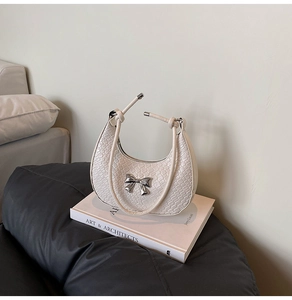 Detail of cream crescent bag with woven texture and a silver metal bow on a book