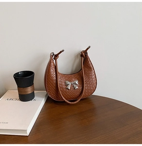 Detail of a brown crescent-shaped handbag with woven texture and a silver bow accessory