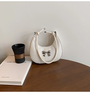 Detailed view of white woven crescent bag with silver bow accent and knotted strap