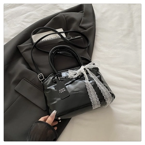 Détail du sac coquille noir brillant avec nœud en dentelle blanche et bandoulière