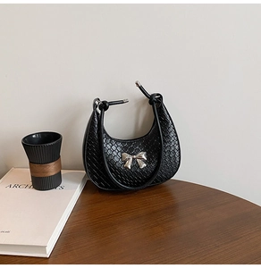 Detail of black crescent shoulder bag featuring crocodile texture and silver metal bow