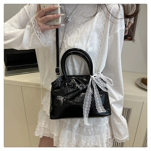 Détail du sac coquille noir avec nœud en dentelle blanche et pieds en métal à la base