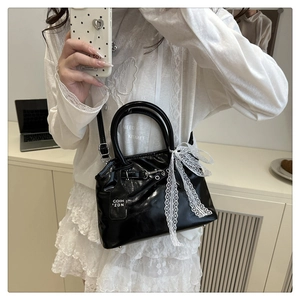 Détail du sac en cuir verni noir avec un nœud en dentelle blanche et une étiquette