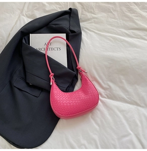 Detailed view of magenta crescent bag with woven texture on white fabric and blazer